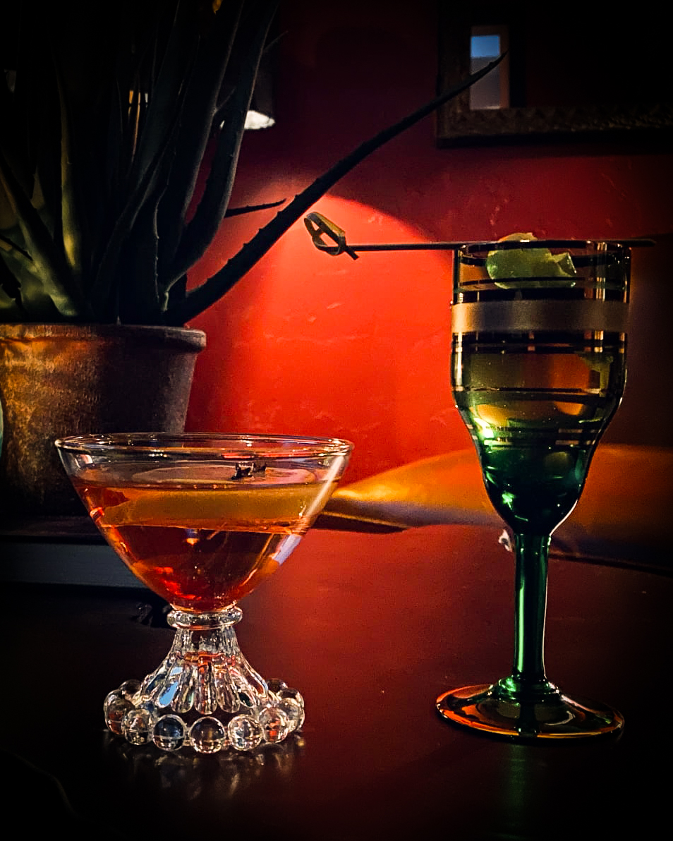 Two cocktails sit on a dark table. 