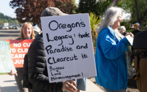 A protester holds a sign that reads — Oregon's Legacy: Took Paradise and Clear Cut it. Bureau of Land Mismanagement.